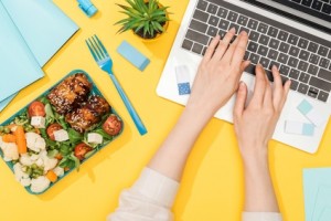 cropped view of woman working with laptop near lunch box and office supplies