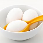 Three eggs in a bowl with one egg resting in an egg holder.