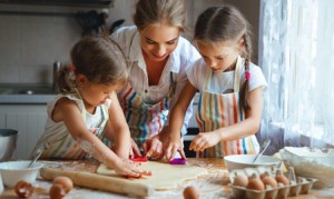 Happy family mother and children twins daughter bake kneading dough in the kitchen