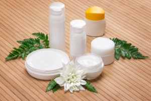 Jars of cream with white flower and fern leaves on wooden surface