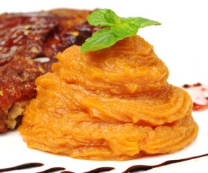 A pile of orange sweet potato puree with a mint leaf on top (Selective Focus, Focus on front of the puree and the front leaf)